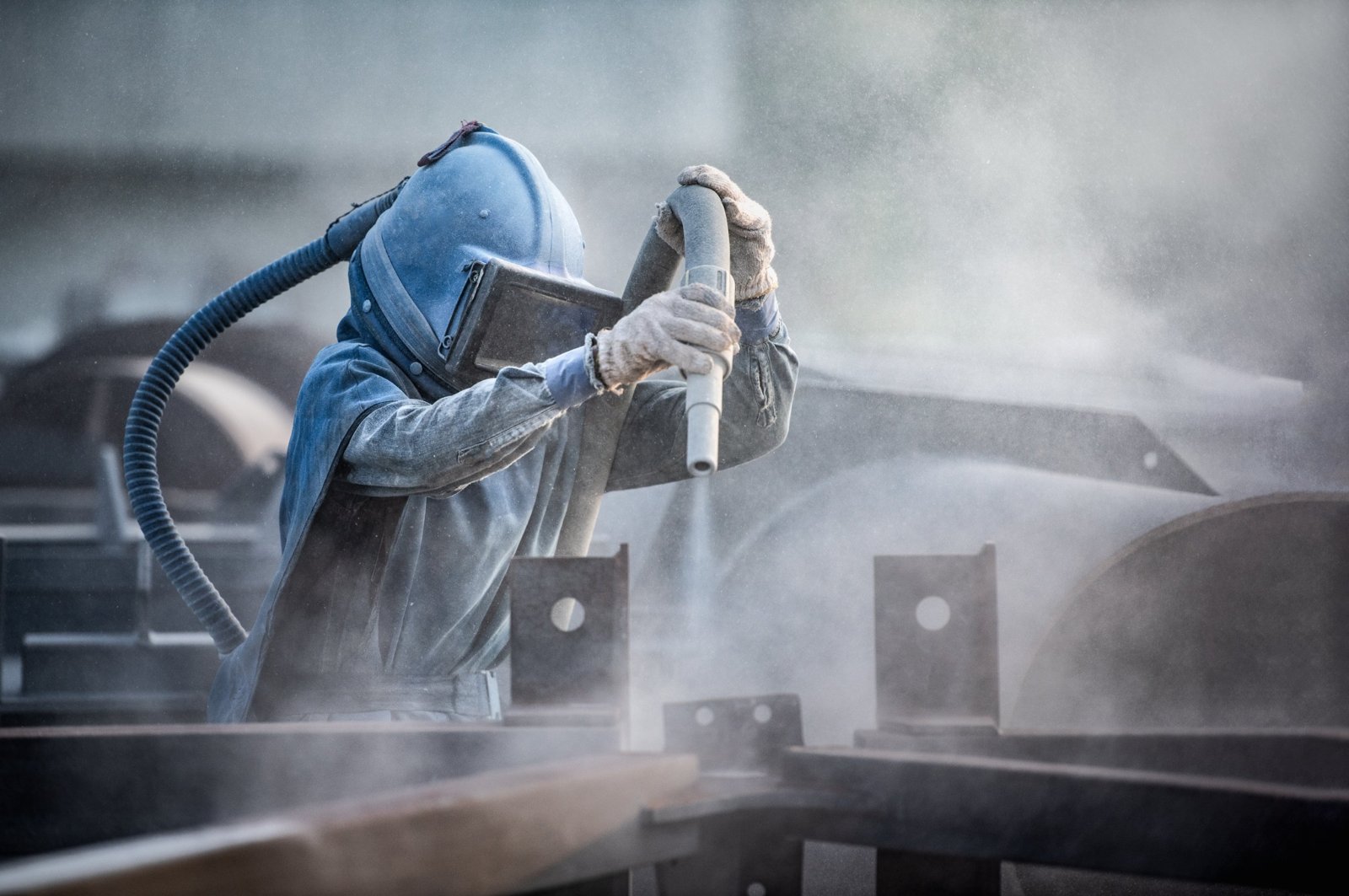 Sandblaster in a blast helmet stripping steel, with grit spraying from the nozzle