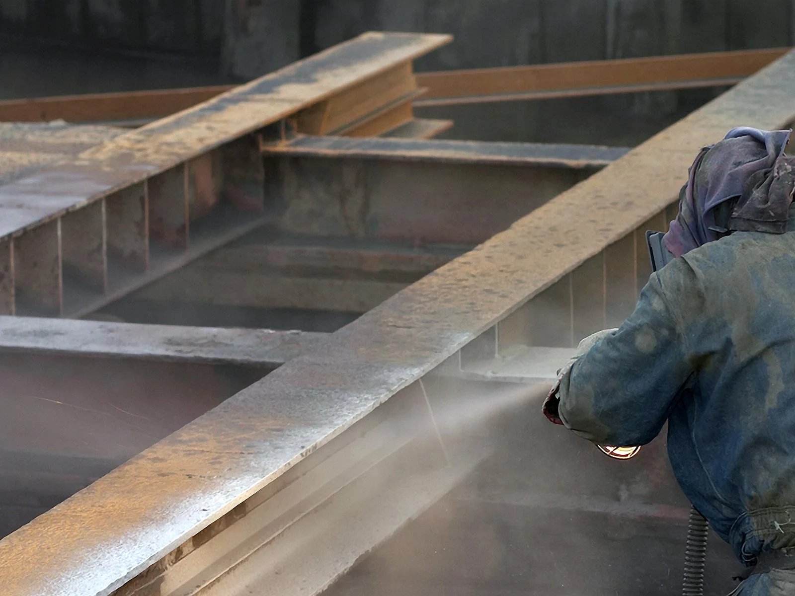 Sandblaster stripping rust from large steel beams